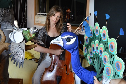 Woman holds cello behind pigeon and peacock puppets