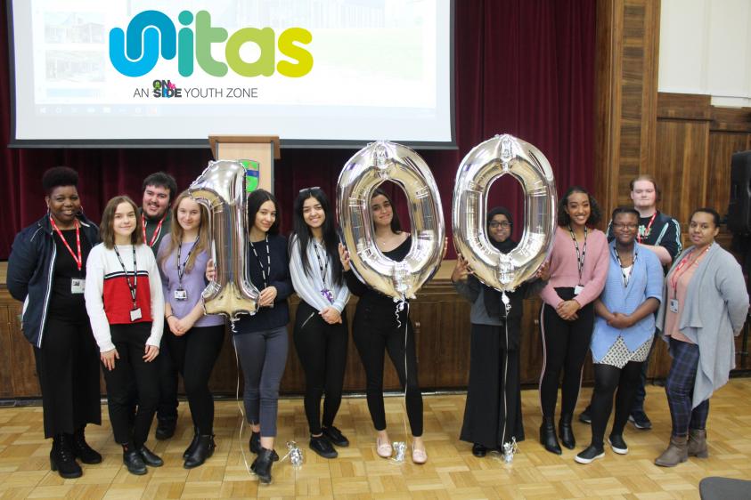 Young people holding balloons balloons spelling 100