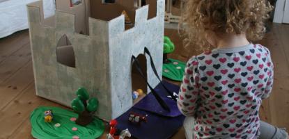 Small child seated on floor in front of a castle made of cardboard